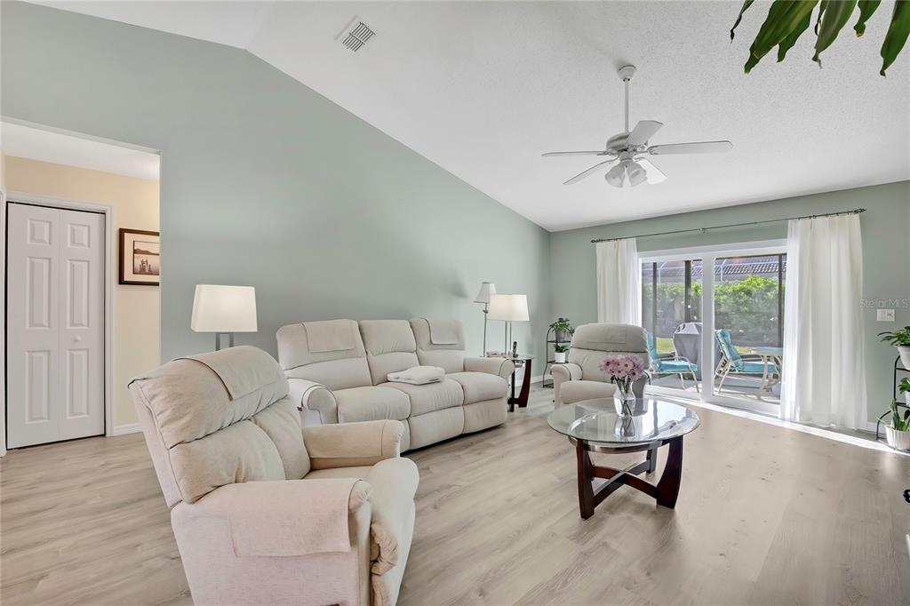 A living room features light wood-look flooring, a vaulted ceiling, and a sliding glass door — 7274 ALOE DRIVE, SPRING HILL, FL