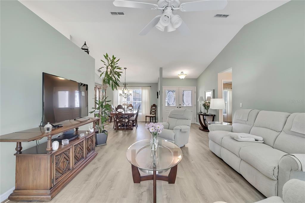 A living room with light green walls, wood-look flooring, a white sofa, and a dining area — 7274 ALOE DRIVE, SPRING HILL, FL