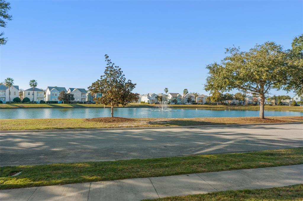A view of a neighborhood pond with a fountain, trees, and houses in the background — 1531 FAIRVIEW CIRCLE, REUNION, FL
