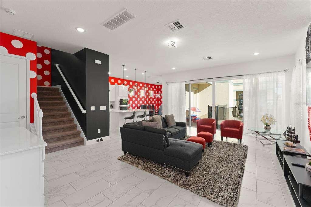 A living room with a Minnie Mouse-themed wall, dark sectional sofa, and white tile floors — 1531 FAIRVIEW CIRCLE, REUNION, FL