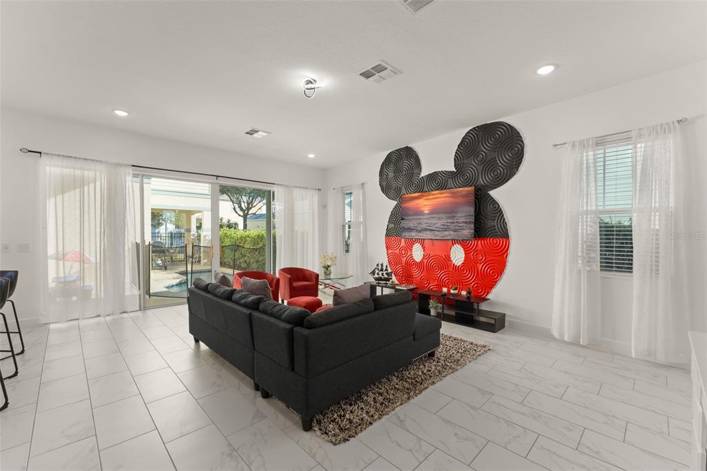 A living room features white tile floors, a dark sectional, and a Mickey Mouse wall feature — 1531 FAIRVIEW CIRCLE, REUNION, FL