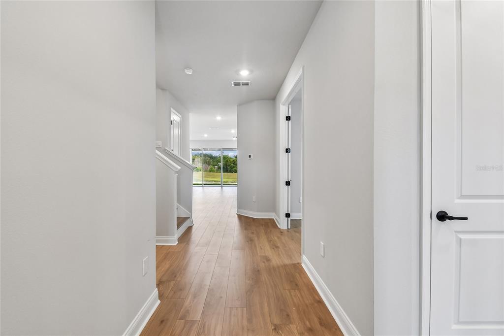 A hallway with light wood flooring leads toward a bright living area with large windows — 5735 LEAFLET TRAIL, MOUNT DORA, FL