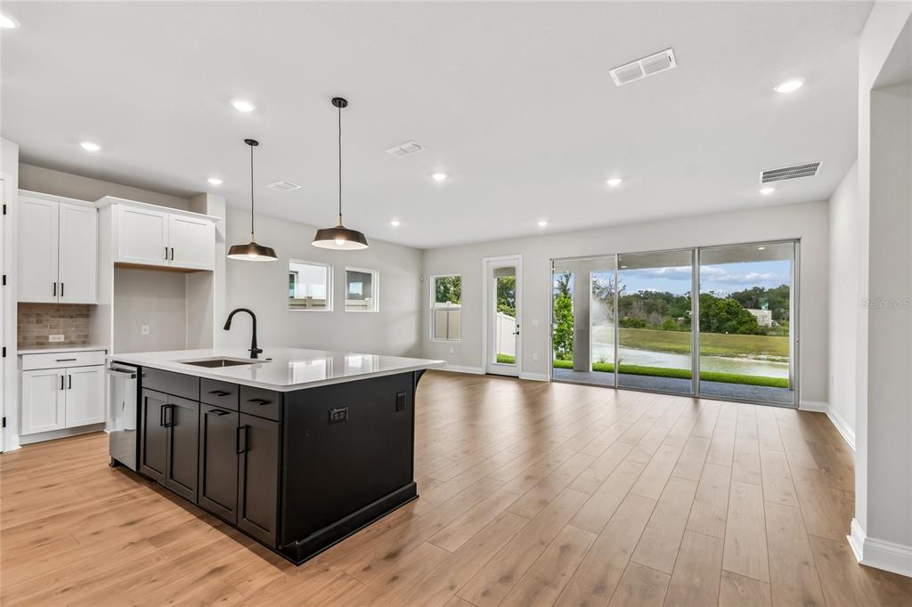 A modern kitchen with a dark island and white cabinets opens to a living area — 5735 LEAFLET TRAIL, MOUNT DORA, FL