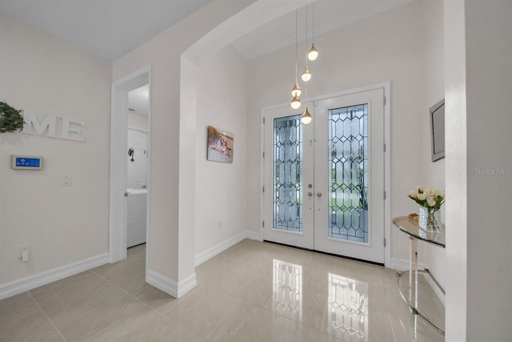 A bright foyer features light tile flooring, double glass-paneled entry doors, and a modern pendant light — 60 FLOYD AVENUE S, LEHIGH ACRES, FL
