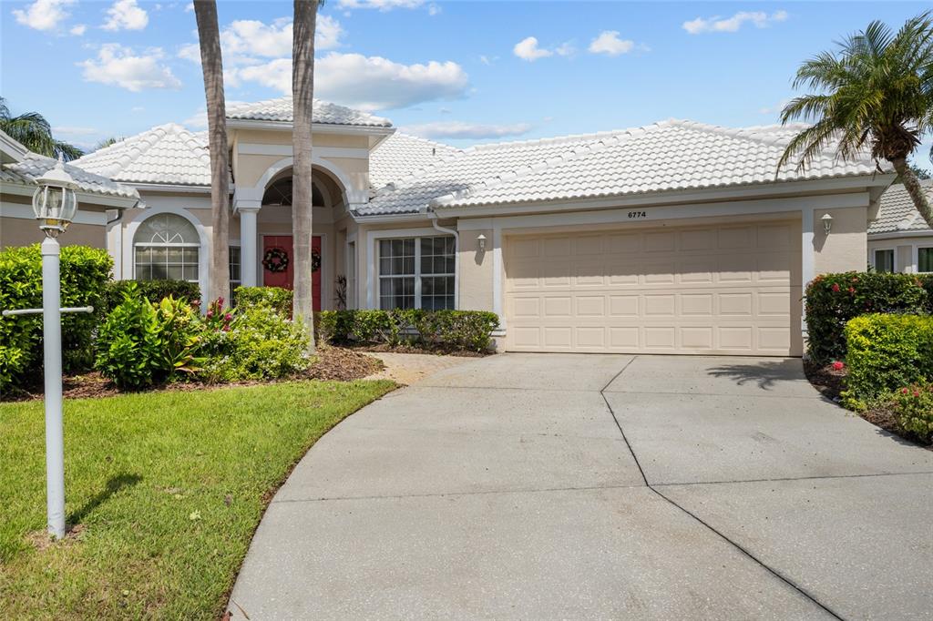 A paved walkway leads to the red double front doors of a beige stucco house — 6774 PASEO CASTILLE, SARASOTA, FL