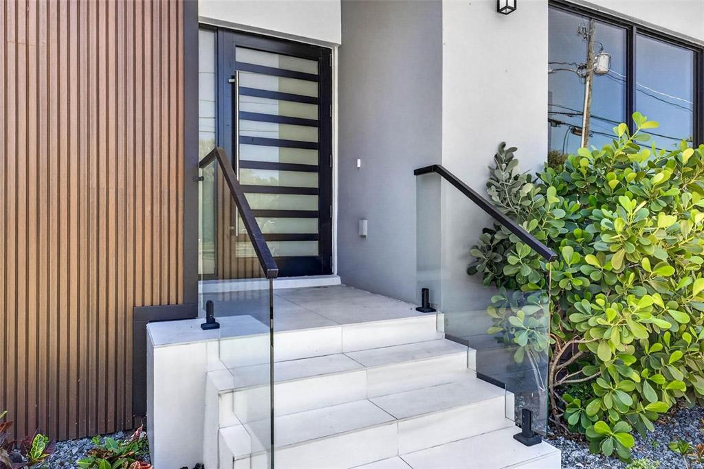 A modern home entrance features white tiled steps, glass railings, and a slatted wood wall — 4426 W EUCLID AVENUE, TAMPA, FL