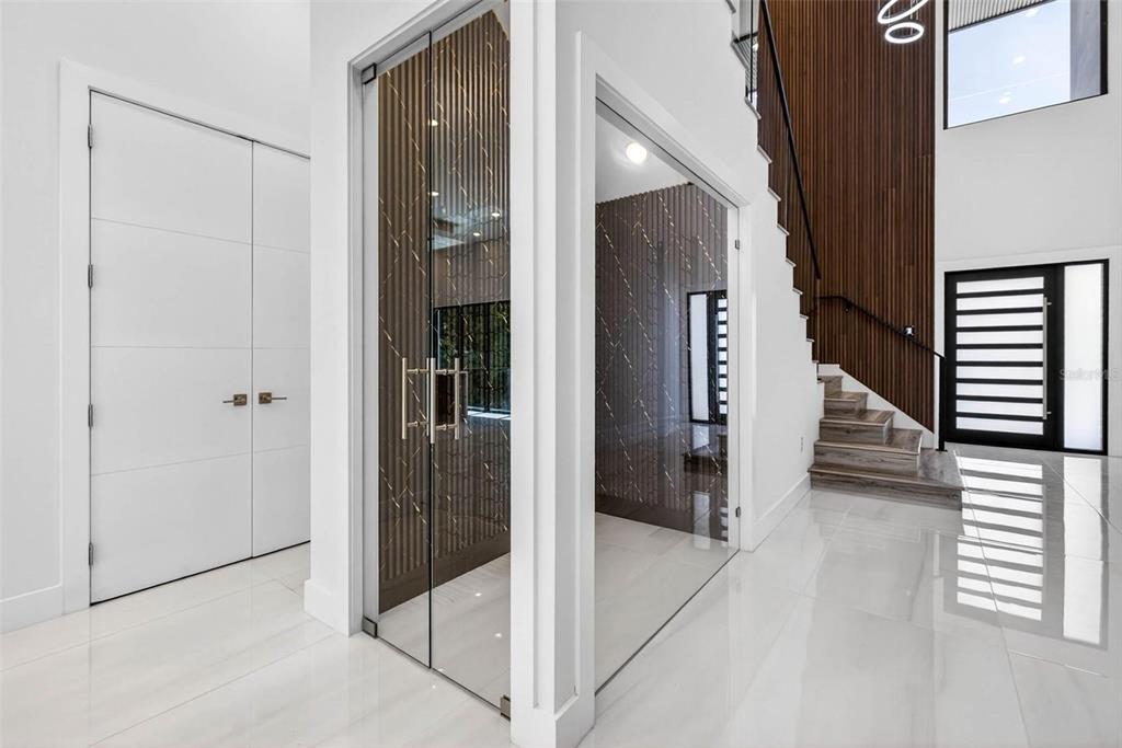 A modern entryway features a glass-enclosed wine cellar, white tile floors, and a wooden staircase — 4426 W EUCLID AVENUE, TAMPA, FL