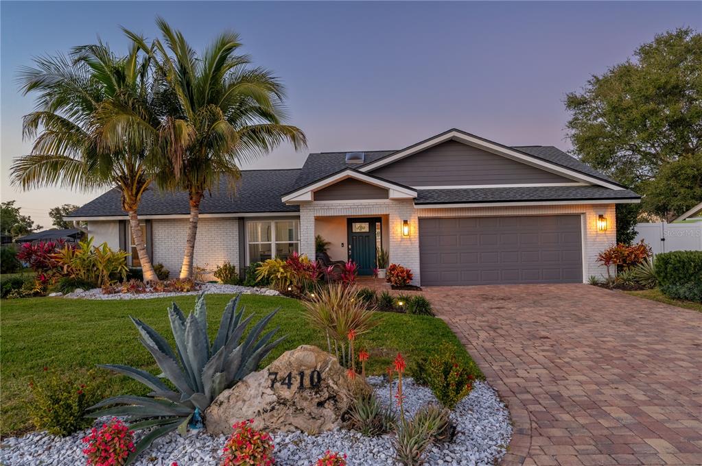 A single-story house with a brick facade, gray siding, a paved driveway, and palm trees — 7410 2ND AVENUE NW, BRADENTON, FL