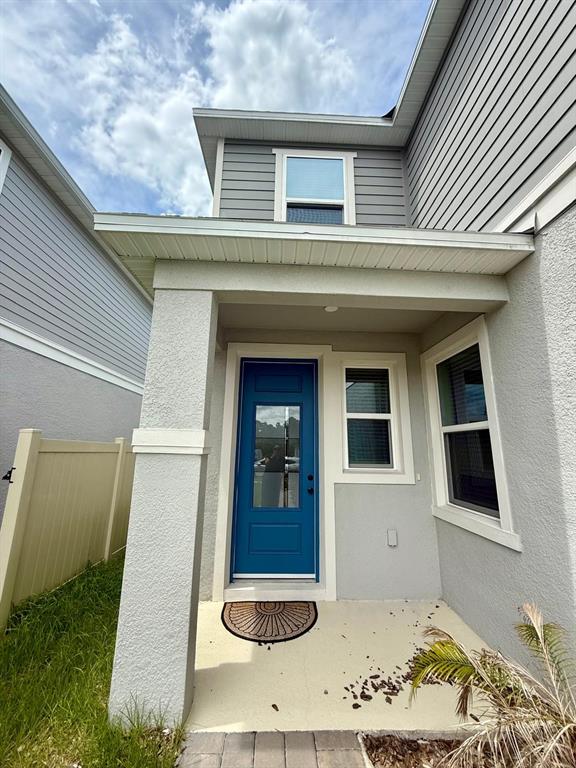A blue front door is centered under a covered porch with gray siding and stucco — 16522 BROOK ISLE WAY, CLERMONT, FL