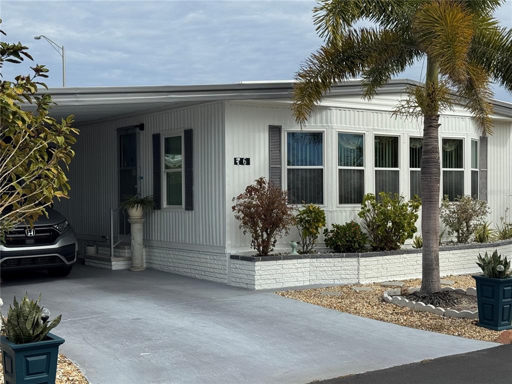 A white mobile home with a carport, gray shutters, and a palm tree in front — 6 LAFITTE DRIVE, NOKOMIS, FL