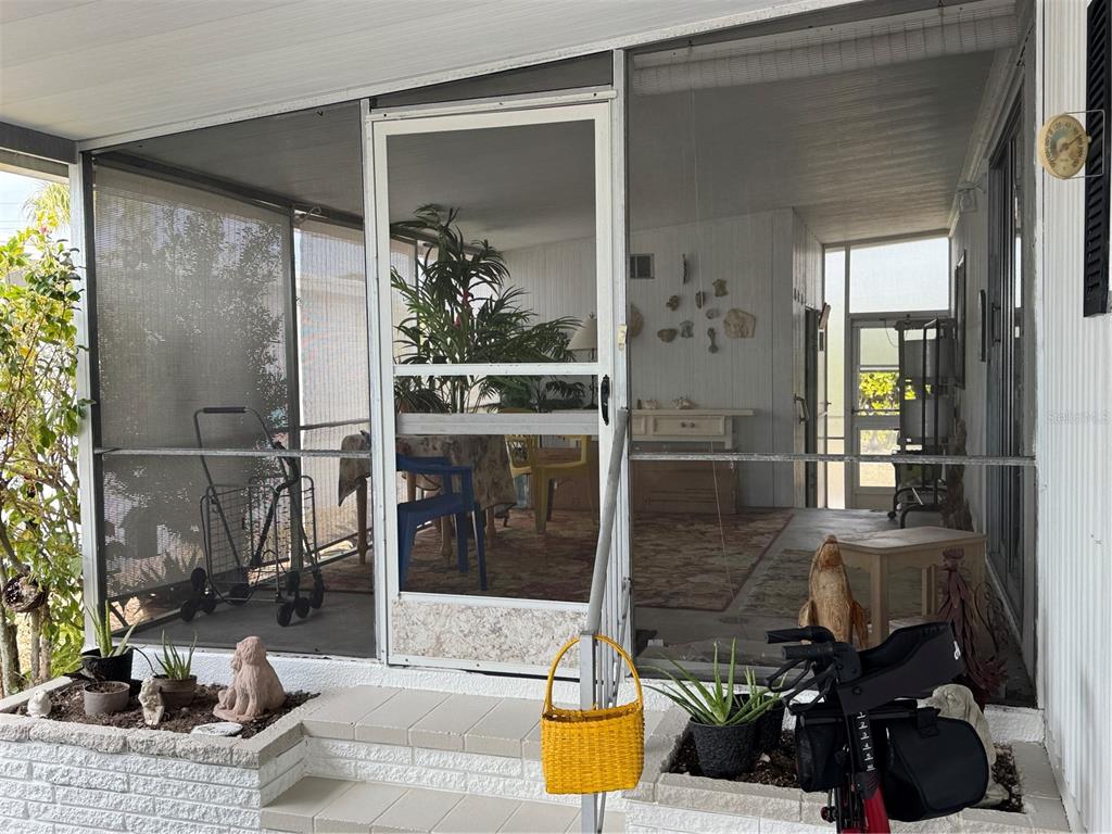 A screened-in porch features a white screen door, tiled flooring, and potted plants — 6 LAFITTE DRIVE, NOKOMIS, FL