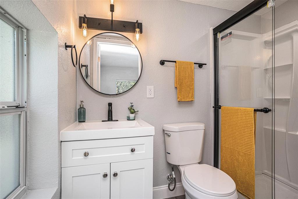 A bathroom features a white vanity, a round mirror, a toilet, and a glass-enclosed shower — 503 PRADO PLACE, LAKELAND, FL