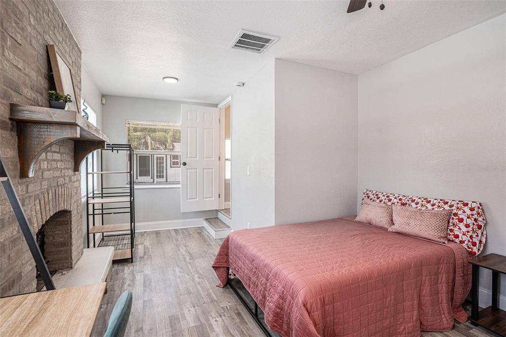 A bedroom features a brick fireplace, wood-look flooring, a bed with a pink quilt, and a doorway — 503 PRADO PLACE, LAKELAND, FL