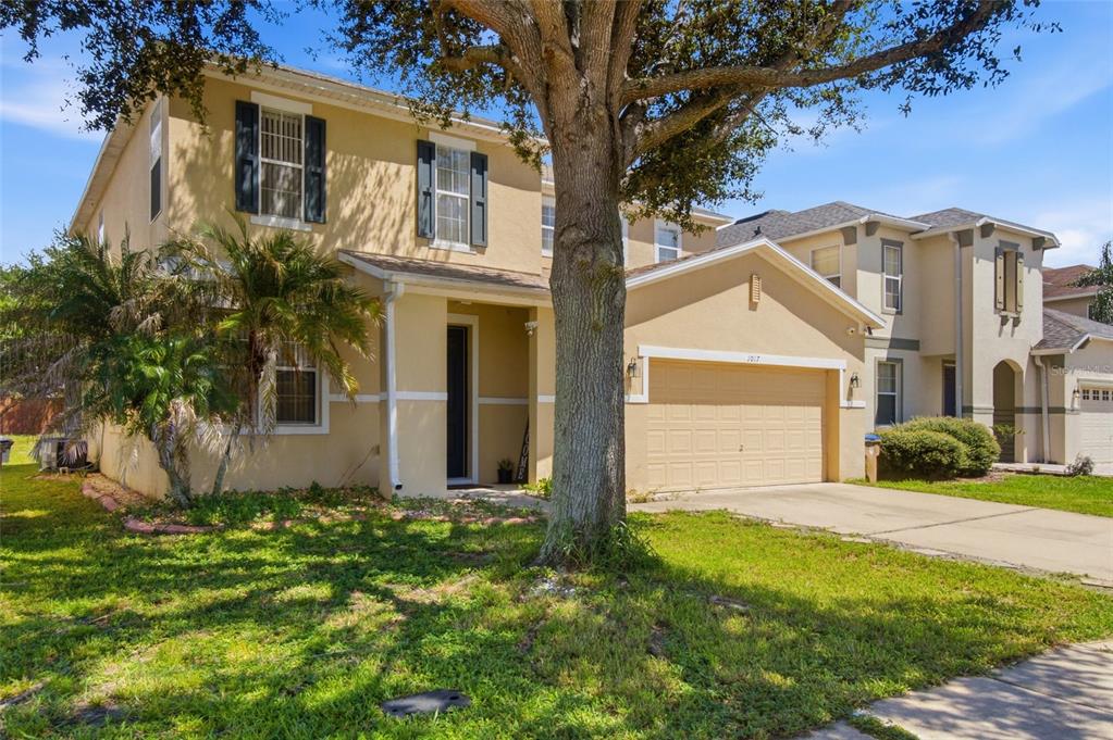 A two-story tan house with a two-car garage and a large tree in the yard — 1017 BERKELEY DRIVE, KISSIMMEE, FL