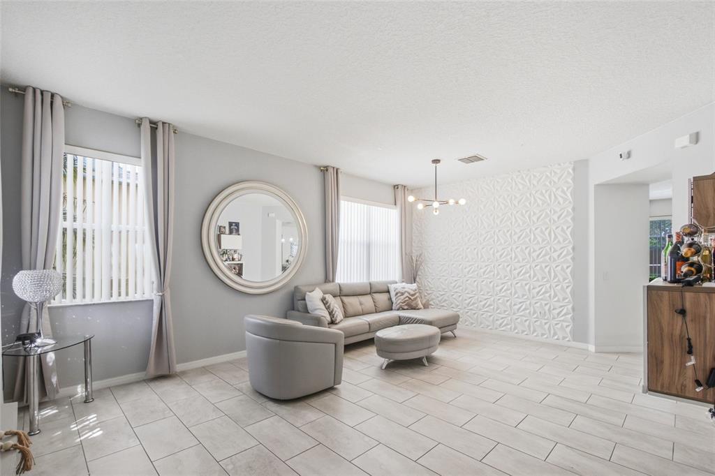 A living room features light gray walls, tile flooring, a sectional sofa, and textured wall panels — 1017 BERKELEY DRIVE, KISSIMMEE, FL