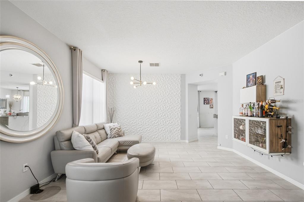 A living room features a grey sectional sofa, a textured accent wall, and a bar cabinet — 1017 BERKELEY DRIVE, KISSIMMEE, FL