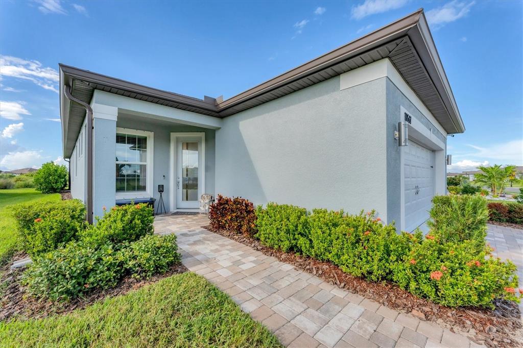 A light blue house exterior features a paved walkway leading to a glass-paneled front door — 10661 SPRING TIDE WAY, PARRISH, FL