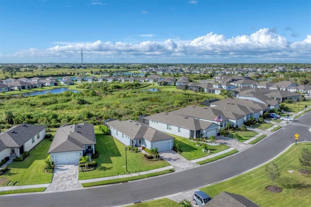 An aerial view shows a suburban neighborhood with single-family homes, paved streets, and green space — 10661 SPRING TIDE WAY, PARRISH, FL