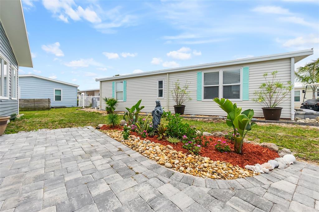 A paved patio sits in front of a mobile home with a landscaped garden bed — 30 WINDWARD DRIVE, FLAGLER BEACH, FL