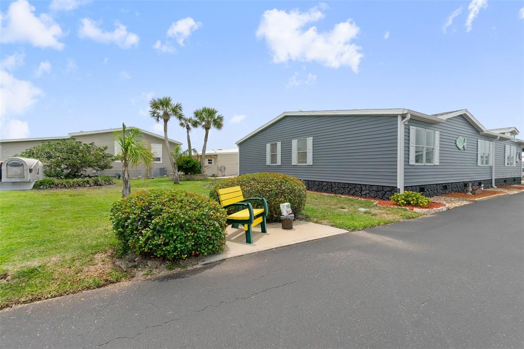 A yellow bench sits on a concrete pad next to a gray manufactured home — 30 WINDWARD DRIVE, FLAGLER BEACH, FL