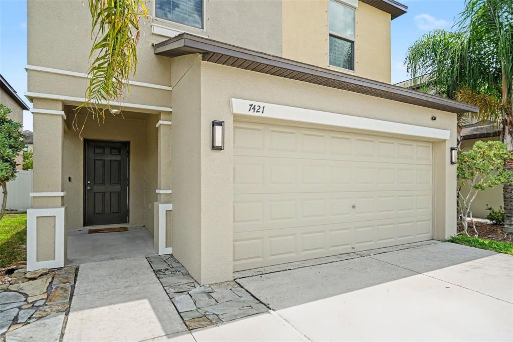 A two-story suburban house with a beige stucco exterior, a two-car garage, and palm trees — 7421 FRENCH MARIGOLD AVENUE, TAMPA, FL