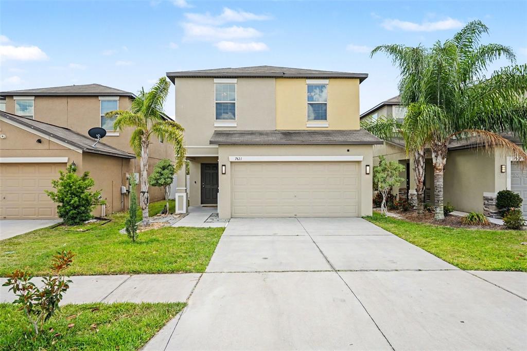 A two-story house exterior features a beige stucco facade, a dark front door, and garage — 7421 FRENCH MARIGOLD AVENUE, TAMPA, FL