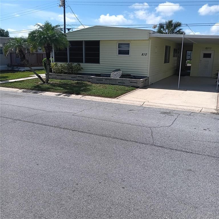A light-yellow mobile home features a screened-in porch, a paved walkway, and landscaping — 810 49TH AVENUE W, BRADENTON, FL