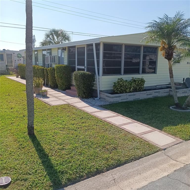 A light yellow mobile home features a concrete driveway, a carport, and a small front yard — 810 49TH AVENUE W, BRADENTON, FL