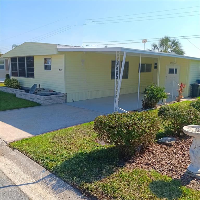 A light yellow mobile home features a white door, paved walkways, and a palm tree — 810 49TH AVENUE W, BRADENTON, FL