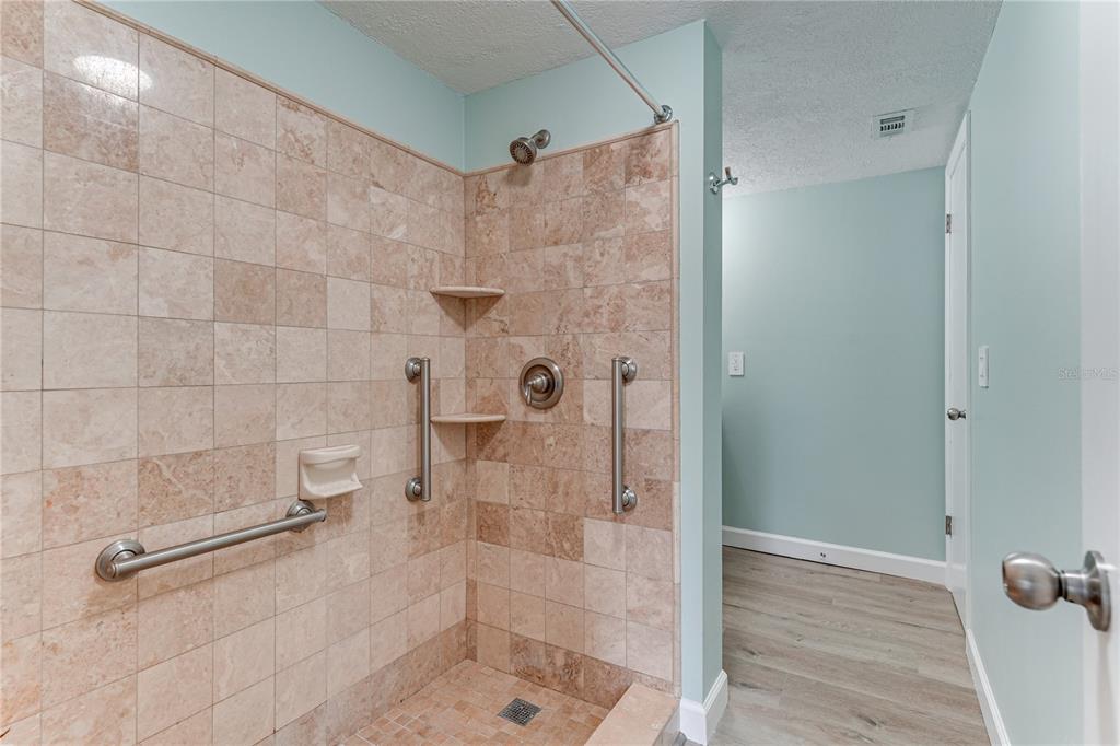 A tiled walk-in shower with grab bars and a showerhead is adjacent to a hallway — 4242 HERON WAY UNIT B323, BRADENTON, FL