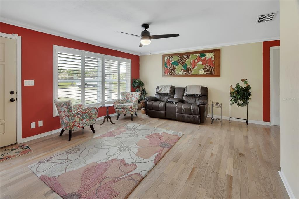 A living room features light wood floors, a red accent wall, and a floral rug — 1610 JUNO TRAIL, ASTOR, FL