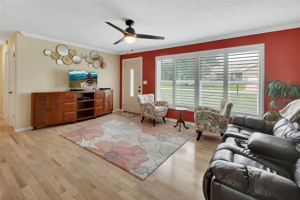 A living room features light wood floors, a red accent wall, and a floral area rug — 1610 JUNO TRAIL, ASTOR, FL
