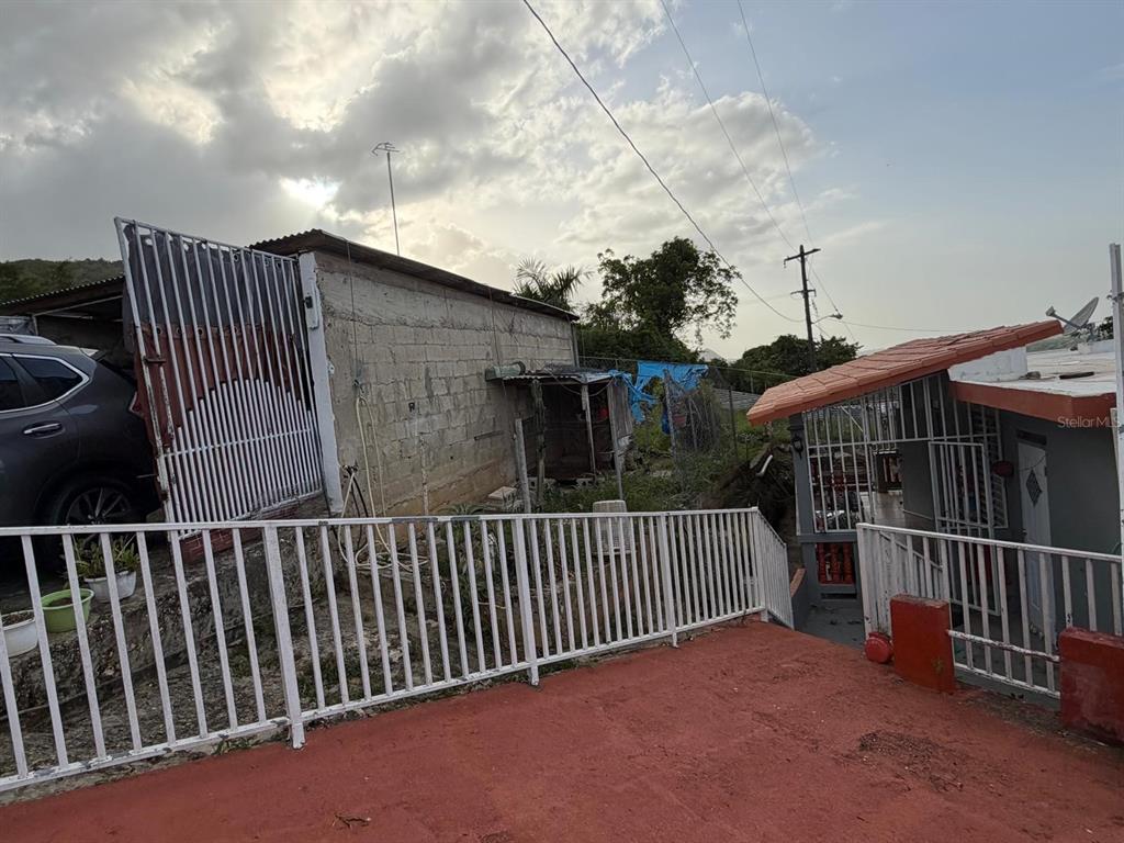 An exterior view shows a concrete building, a metal gate, and a red-painted patio area — Carr. 10 BO. HATO VIEJO, ARECIBO, PR