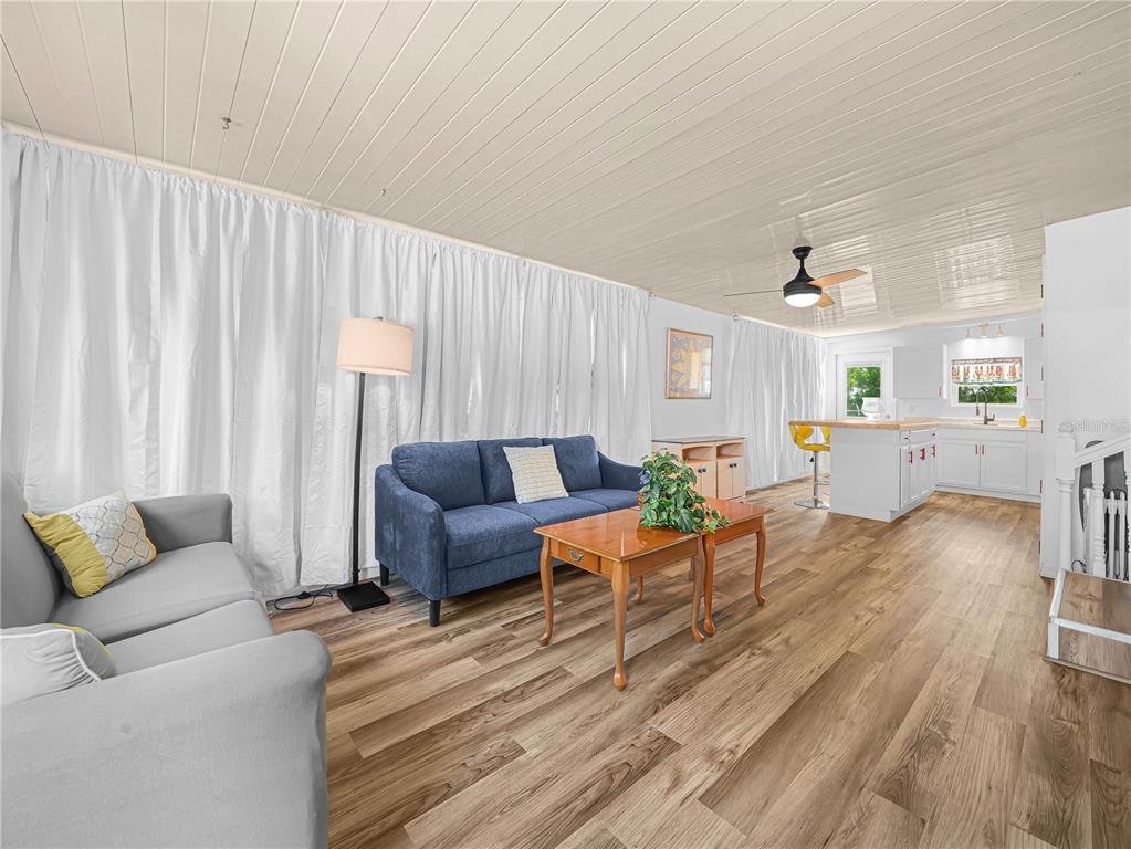 A living room with wood-look flooring, a blue sofa, and an open kitchen in back — 40 SADDLEBAG TRAIL N, LAKE WALES, FL