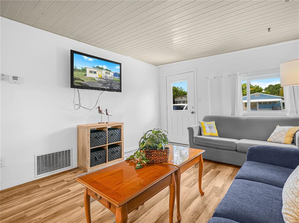 A living room features wood-look flooring, a grey sofa, a wooden coffee table, and a television — 40 SADDLEBAG TRAIL N, LAKE WALES, FL