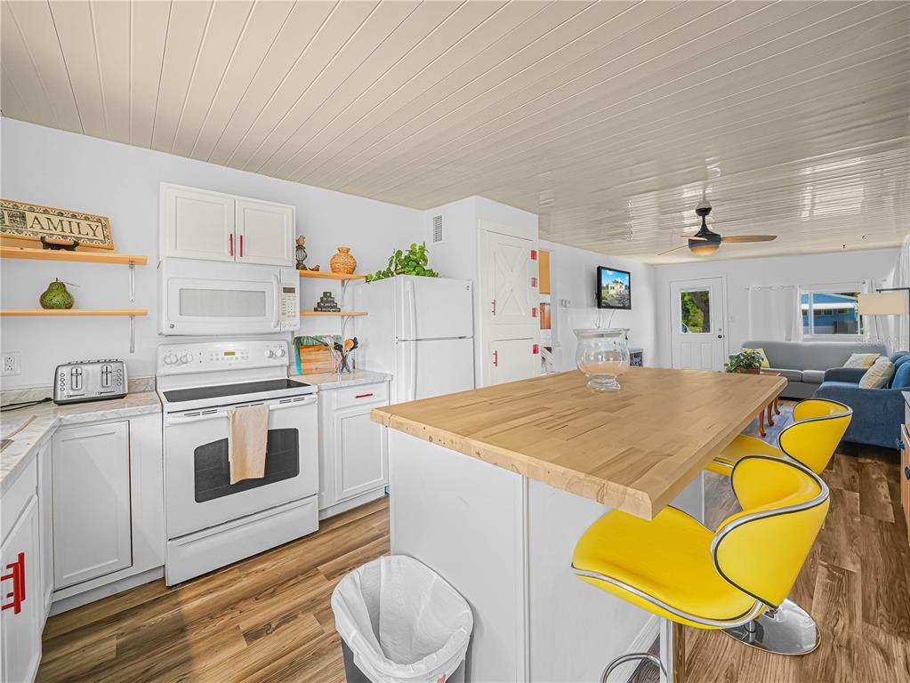 A kitchen features white cabinets, a wooden island with yellow stools, and wood-look flooring — 40 SADDLEBAG TRAIL N, LAKE WALES, FL