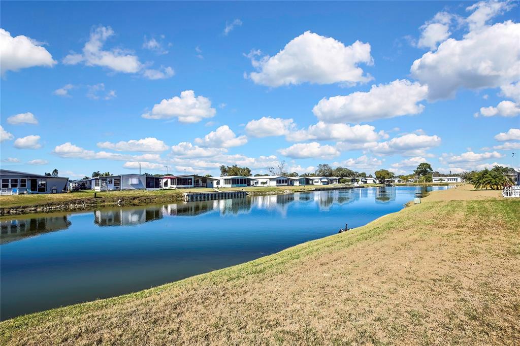 A canal runs alongside a row of manufactured homes under a bright, cloudy sky — 3141 NANTUCKET DRIVE, HOLIDAY, FL