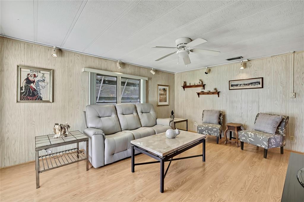A living room features wood-paneled walls, light wood flooring, a gray sofa, and two chairs — 3141 NANTUCKET DRIVE, HOLIDAY, FL