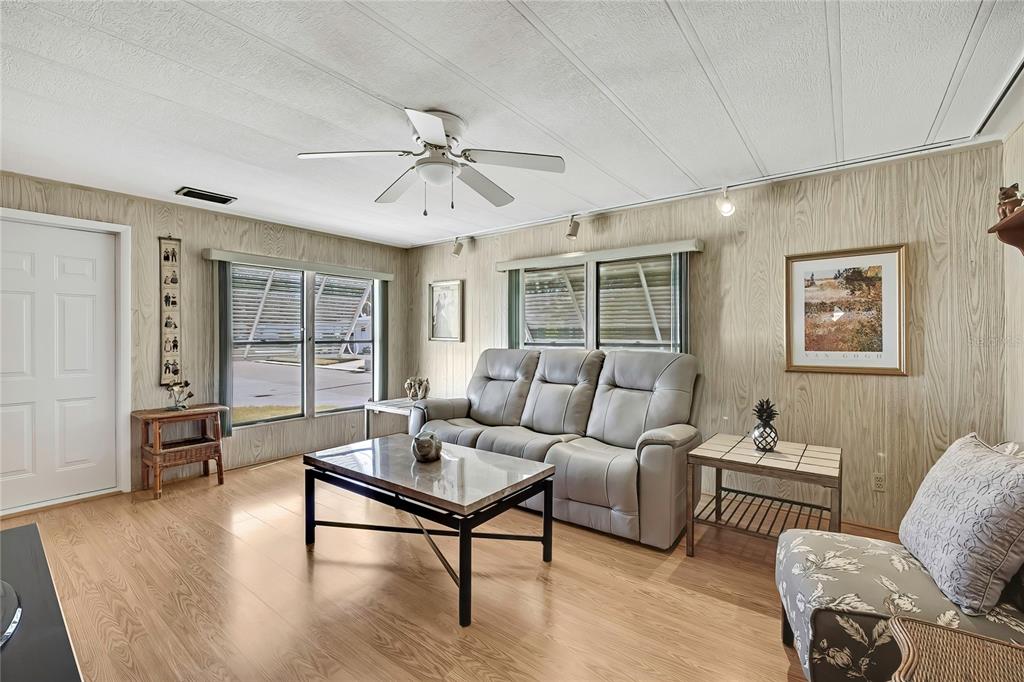 A living room features wood-paneled walls, light wood flooring, a gray sofa, and a ceiling fan — 3141 NANTUCKET DRIVE, HOLIDAY, FL