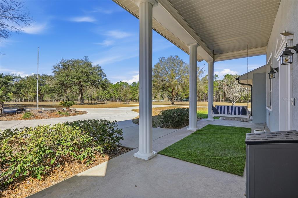 A covered porch features white columns, a hanging bench, and a patch of artificial turf — 9115 NW 170TH STREET, ALACHUA, FL