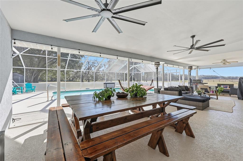 A covered patio features a wooden picnic table, ceiling fans, and a screened-in swimming pool — 9115 NW 170TH STREET, ALACHUA, FL