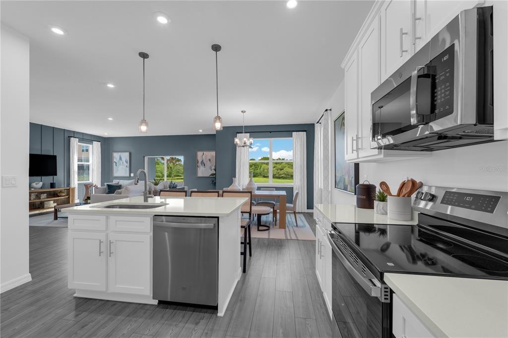 A modern kitchen with white cabinets and a stainless steel island overlooks an open living area — 10067 MORNING MEADOWLARK TRAIL, PARRISH, FL