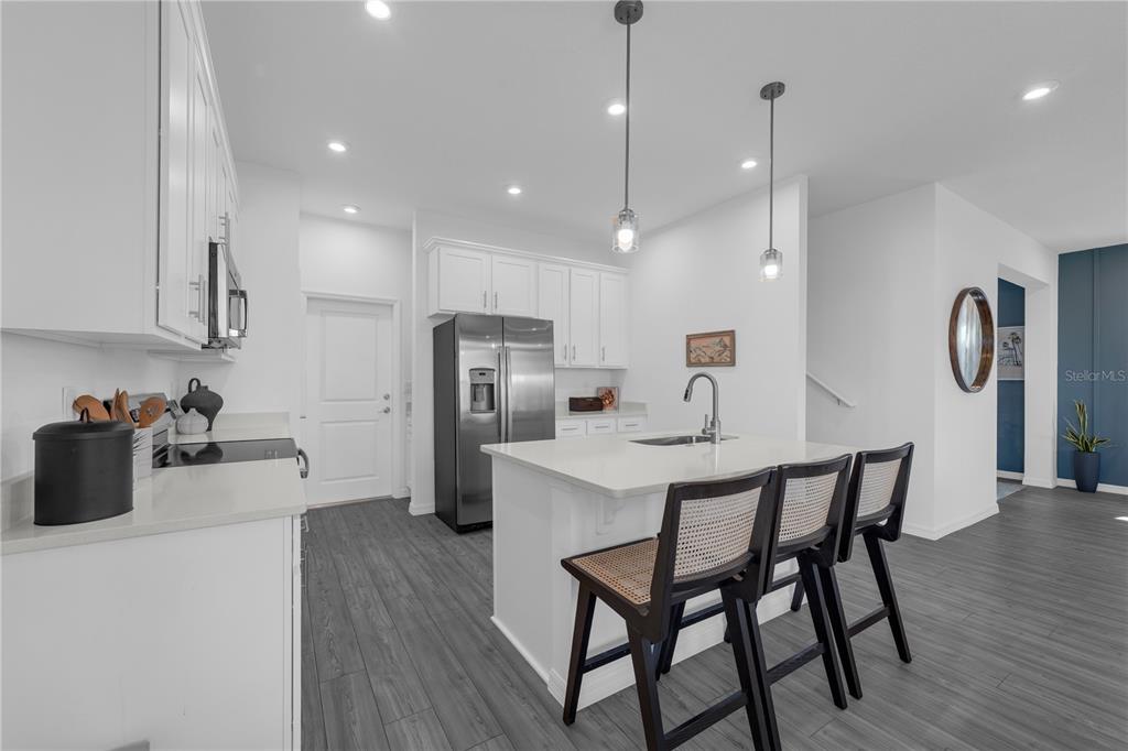 A modern kitchen features white cabinetry, a central island with bar stools, and gray flooring — 10067 MORNING MEADOWLARK TRAIL, PARRISH, FL