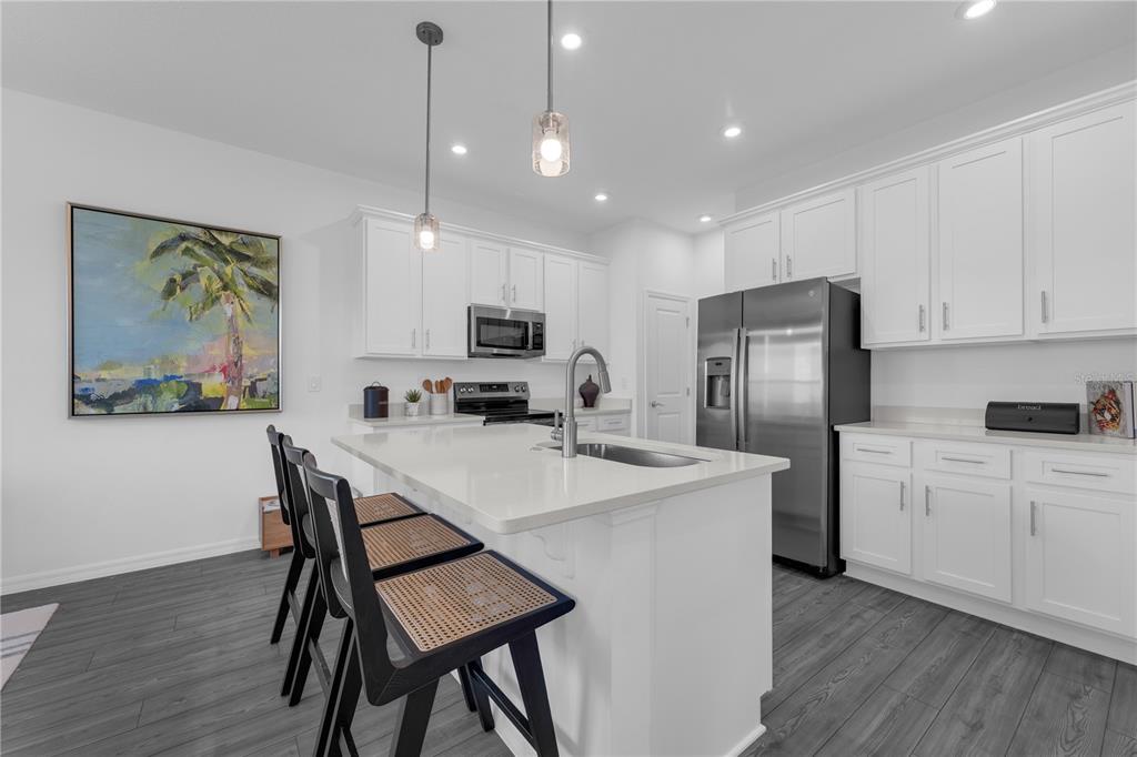 A modern kitchen features white cabinetry, a central island with bar seating, and stainless appliances — 10067 MORNING MEADOWLARK TRAIL, PARRISH, FL