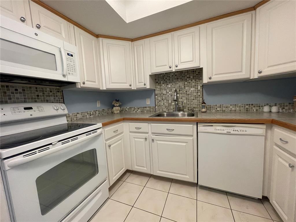 A kitchen features white cabinets, a tiled backsplash, a white stove, and a dishwasher — 625 MIDWAY DRIVE UNIT A, OCALA, FL