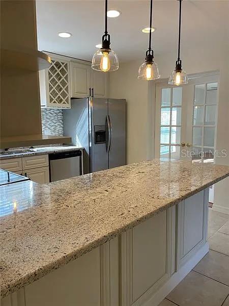 A kitchen features a granite-topped island, stainless steel appliances, and three pendant lights — 1424 CHESTERFIELD DRIVE, DUNEDIN, FL