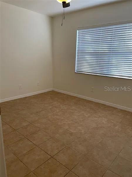 An empty room features beige tile flooring, off-white walls, and a window with horizontal blinds — 1424 CHESTERFIELD DRIVE, DUNEDIN, FL