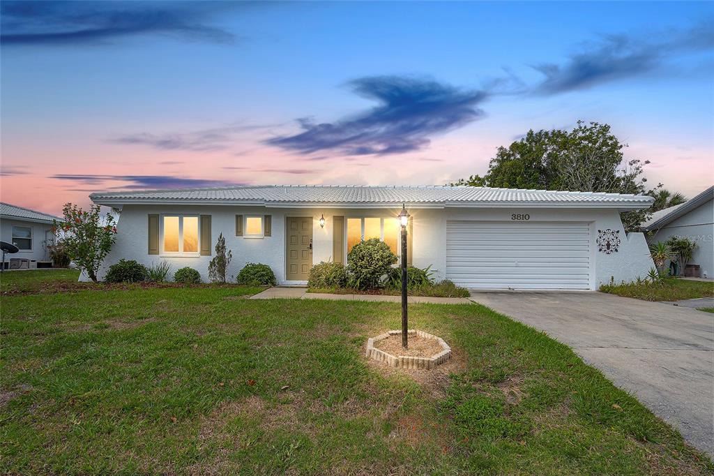 A single-story white house with a garage and a front lawn at dusk — 3810 JOYCE DRIVE, BRADENTON, FL
