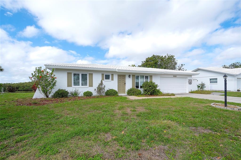 A single-story white house with a garage and a grassy front yard under a cloudy sky — 3810 JOYCE DRIVE, BRADENTON, FL