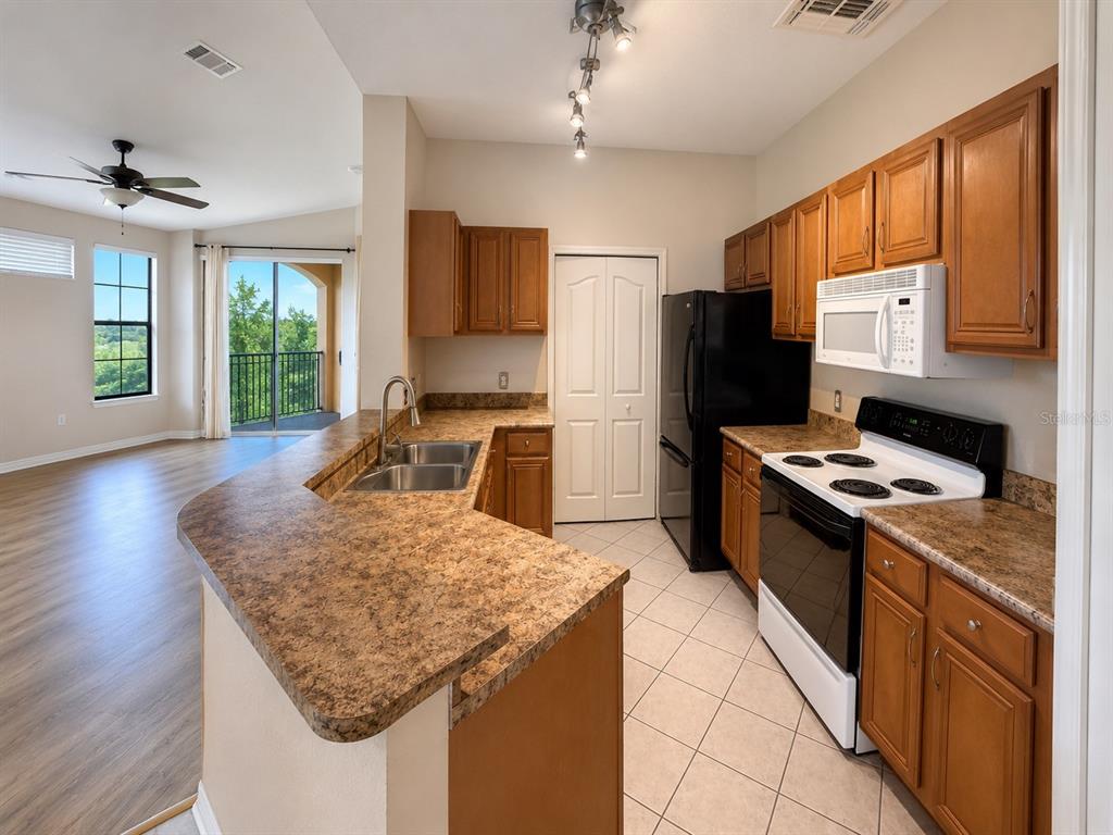 A kitchen with brown cabinets, laminate countertops, and black appliances opens to a living area — 6157 METROWEST BOULEVARD UNIT 308, ORLANDO, FL